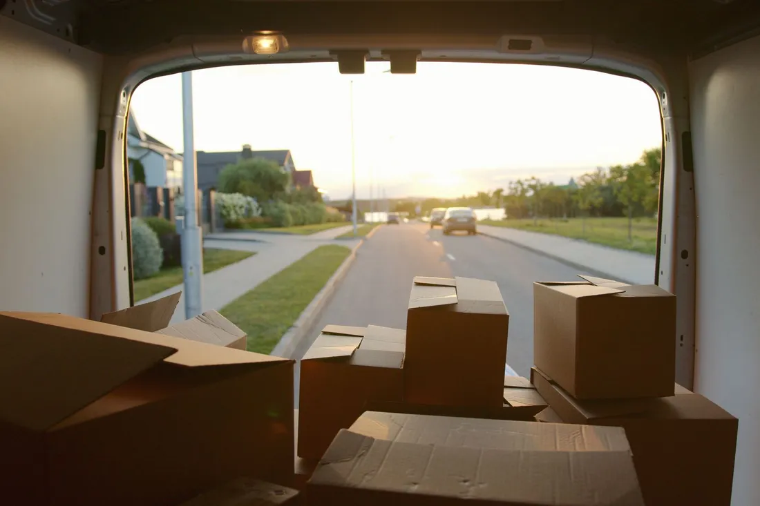 Blick aus dem Laderaum eines Transporters auf gestapelte Umzugskartons, dahinter eine ruhige Wohnstraße im Abendlicht.