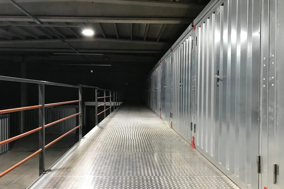 Langer Gang in einer Lagerhalle mit abgeschlossenen Lagerabteilen aus Metall und Riffelblechboden.